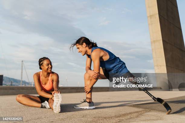 young disabled man with a leg prosthesis stretching after jogging. man and woman practicing stretching. concept of disability. - fake man stockfoto's en -beelden