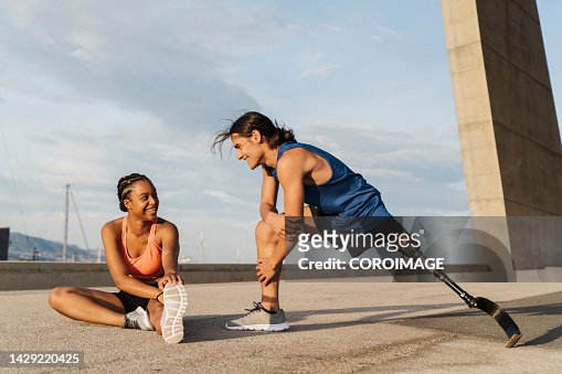Young disabled man with a leg prosthesis stretching after jogging. Man and woman practicing stretching. Concept of disability.