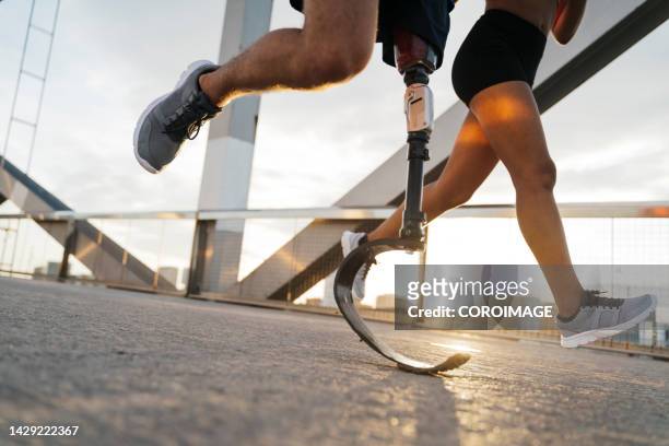 close-up of disabled man running with a prosthetic leg. woman and young man running in the city at sunset. disability and jogging concept. - equipo protésico fotografías e imágenes de stock