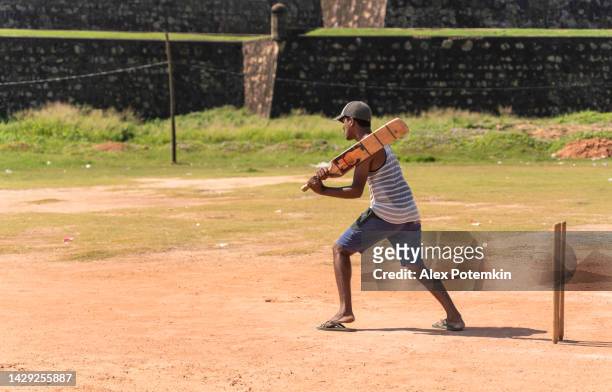 the batsmen of the local street cricket team is defending the base - hitting the ball with a bat  in front of the historic fortress in galle, sri lanka.. - wicket stockfoto's en -beelden
