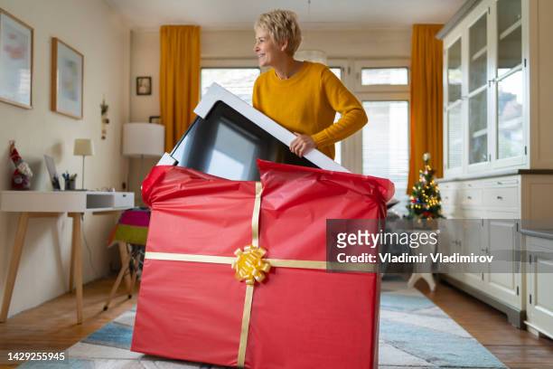 frau mittleren alters freut sich, einen fernseher als weihnachtsgeschenk zu erhalten - gross domestic product stock-fotos und bilder