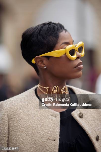 Guest wearing a black top, beige short jacket on the shoulders, golden necklace/choker with the word LOVE, and yellow sunglasses from Loewe outside...