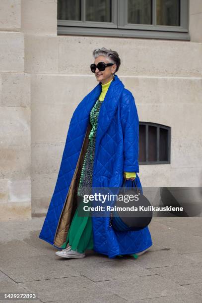 Guest wearing a green long skirt, bright neon yellow, turtle neck top, shiny green short dress on top, long quilted coat, black sunglasses, and black...