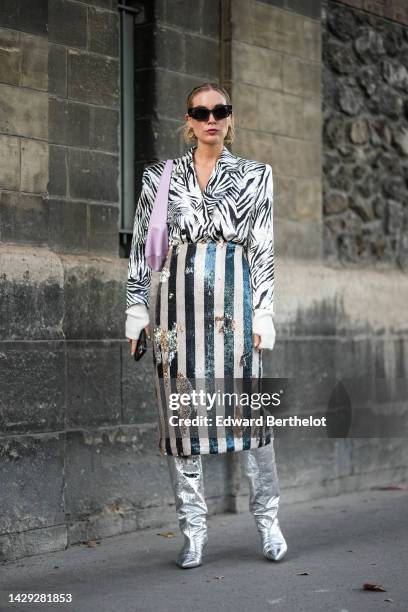 Guest wears black sunglasses, gold earrings, a white with black zebra print pattern blazer jacket, a white and black striped print pattern shiny...