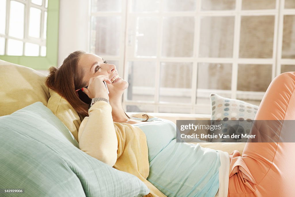 Woman laughing, on mobilephone relaxingon sofa.