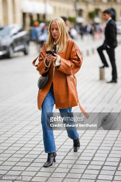 Guest wears a white latte wool pullover, a camel shiny leather oversized jacket, a black shiny leather in shape of heart shoulder bag from Alaia,...