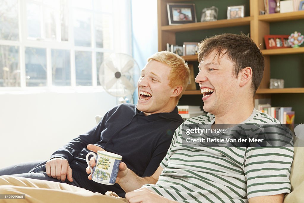 Men laughing watching tv, sitting in livingroom.