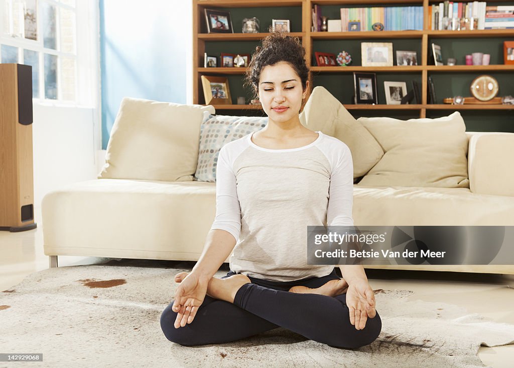 Woman relaxing in yoga pose in livingroom.