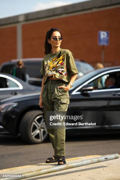 Guest wears black cat eyes sunglasses, a khaki with painted yellow / white / red / black horse pattern t-shirt from Etro, khaki cargo pants, a black...