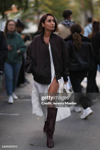 Fashion week guest seen wearing a bomber jacket with a white dress and leather boots, outside Acne Studios during Paris Fashion Week on September 28,...