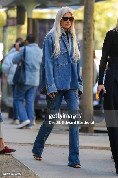 Sarah Harris wears black sunglasses, a blue denim large shirt, blue denim flared pants, black shiny leather strappy heels sandals, a black wool...