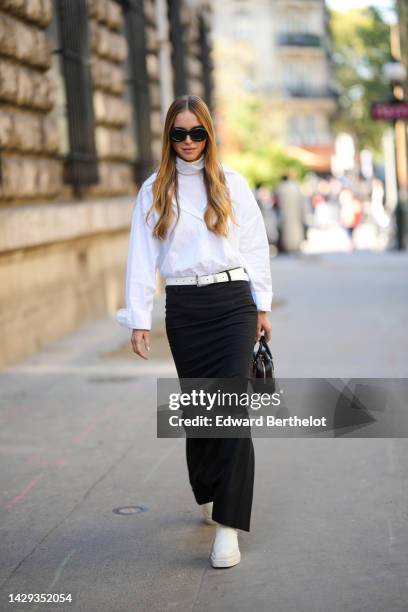 Pernille Teibaek wears black puffy sunglasses from Loewe, a white turtleneck pullover, a white shirt, a white latte shiny leather belt, black slit...