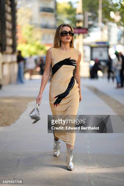 Guest wears brown square sunglasses, earrings, a beige with black hand print pattern sleeveless / long tube dress, a silver shiny leather triangular...