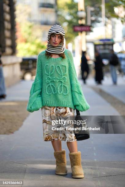 Guest wears a black and white striped print pattern wool hoodie / balaclava, a green oversized wool with embroidered large logo pullover from Loewe,...