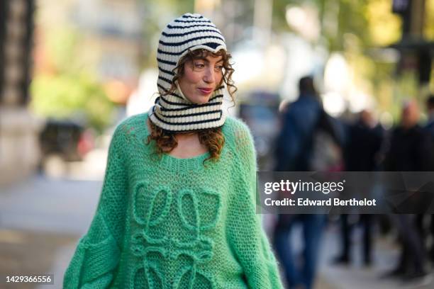 Guest wears a black and white striped print pattern wool hoodie / balaclava, a green oversized wool with embroidered large logo pullover from Loewe,...