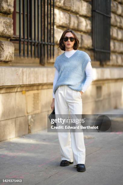 Guest wears brown sunglasses, a white long sleeves t-shirt, a pale blue wool sleeveless pullover, white latte suit pants, a black shiny crocodile...