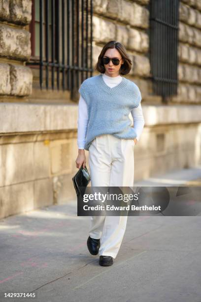 Guest wears brown sunglasses, a white long sleeves t-shirt, a pale blue wool sleeveless pullover, white latte suit pants, a black shiny crocodile...