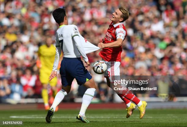 Martin Odegaard of Arsenal and Heung-Min Son of Tottenham Hotspur challenge for the ball during the Premier League match between Arsenal FC and...