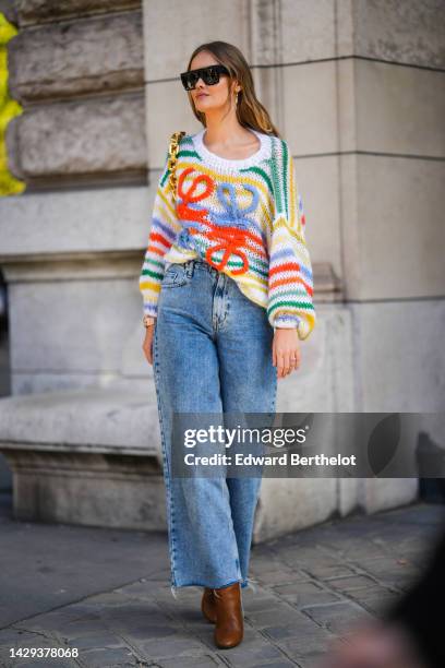 Guest wears black sunglasses, gold earrings, a white with green / yellow / blue striped print pattern with embroidered neon orange and blue logo...