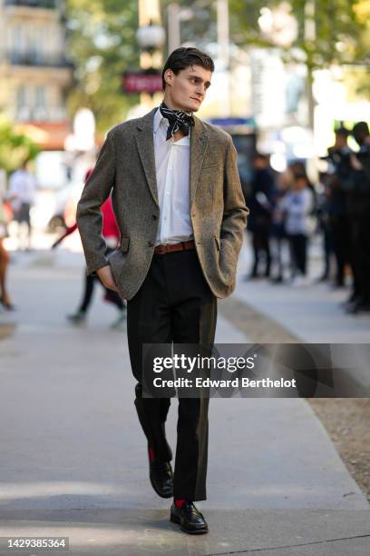 Guest wears a black with white print pattern silk scarf, a white shirt, a brown blazer jacket, a camel shiny leather belt, black suit pants, red...