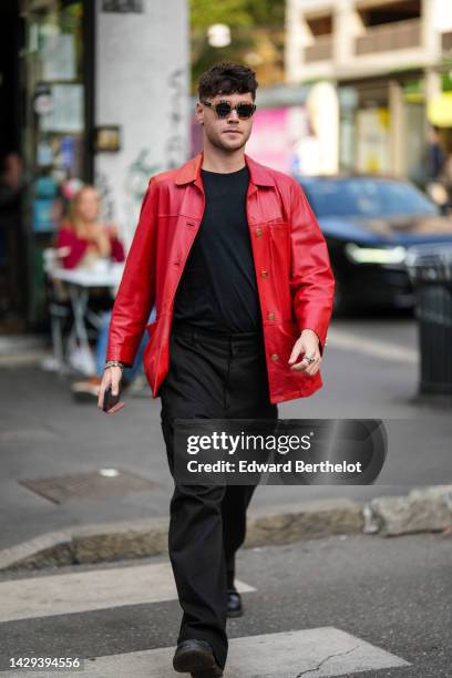 Guest wears black sunglasses, a black t-shirt, black suit pants, a red shiny leather shirt, black shiny leather ankle boots , outside Missoni, during...