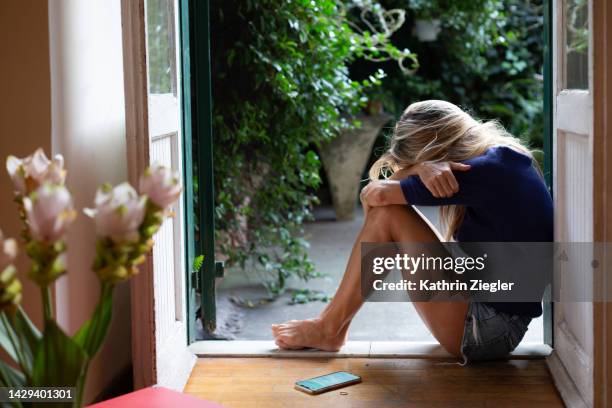 woman crouching down in despair with head on her knees - corazón roto fotografías e imágenes de stock