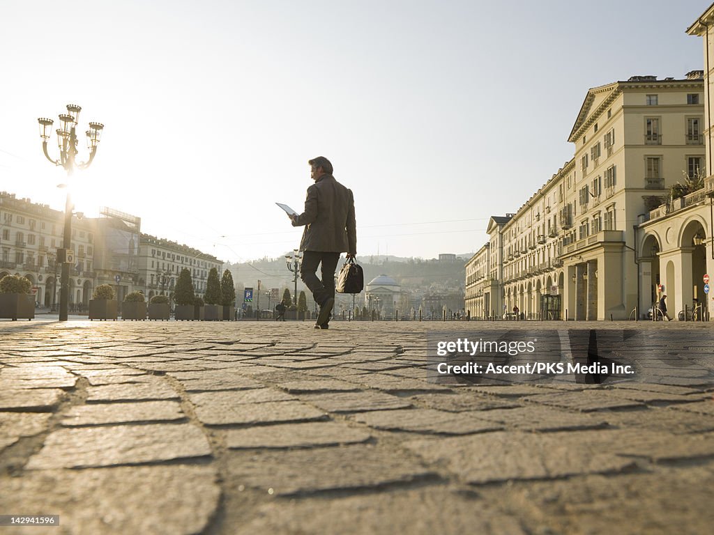 Businessman consults digital tablet,crosses piazza