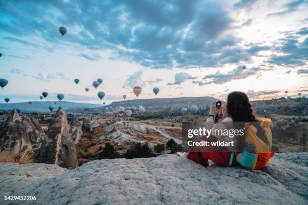 traveler photographer girl takes photo of hot air balloons during sunrise in cappadocia nevsehir , turkey - cappadocië stockfoto's en -beelden