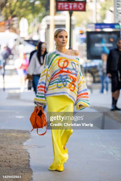 Leonie Hanne wears yellow asymmetric skirt, orange rust brown bag, knitted striped jumper with wide sleeves, heels outside Loewe during Paris Fashion...