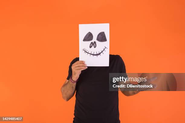 man covering his face with a paper on which a terrifying halloween smiling face is painted, bewildered, on orange background. concept of celebration, day of the dead and carnival. - cover monster face bildbanksfoton och bilder