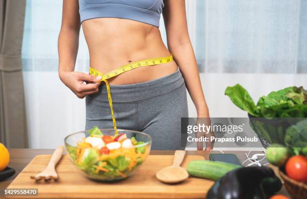 woman measuring her waist - dieta baja en carbohidratos fotografías e imágenes de stock