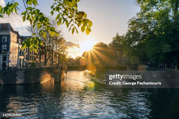 tourist boat in the canals of amsterdam, holland at sunset - netherlands sunset stock pictures, royalty-free photos & images