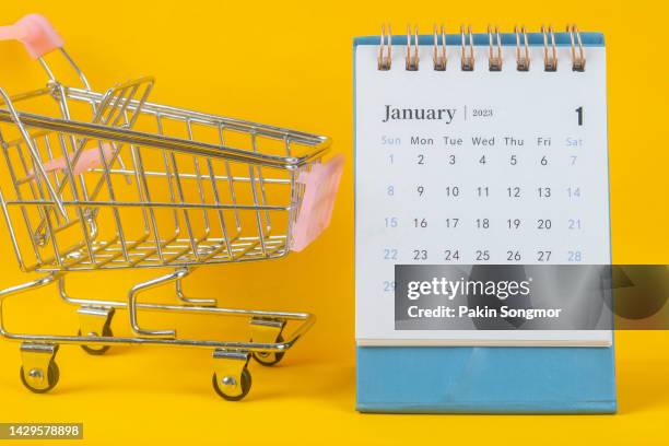 calendar desk 2023: january is the month for the organizer to plan and deadline with a shopping cart against a yellow paper background. - january holiday sale stock-fotos und bilder