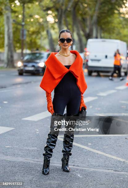 Anna Rosa Vitiello wears orange cape, black over all, over knees boots, necklace, sunglasses outside Akris during Paris Fashion Week - Womenswear...