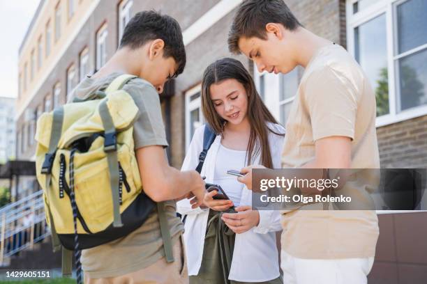 smiling students surfing mobile internet, social net near school, change contacts for meeting - 3 teenagers mobile outdoors stockfoto's en -beelden