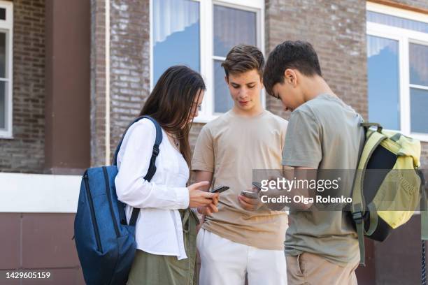 first day in new school. students surfing mobile internet, social net near school, change contacts for meeting - 3 teenagers mobile outdoors stock-fotos und bilder