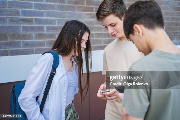 peer pressure and cyberbullying at school. students surfing mobile internet, social net near school - peer pressure stock pictures, royalty-free photos & images