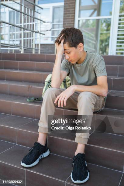 bad grades and teenage fears. depressed teenage boy hiding face with hand, sitting on school steps. - child report card stock pictures, royalty-free photos & images