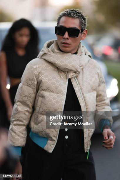 Evan Mock is seen wearing a black large Off-White sunglasses, beige logo pattern Off-White puffer jacket with blue details, black t-shirt and black...