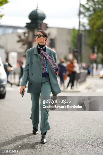 Julia Haghjoo wears black sunglasses, white pearls earrings, ,a black turtleneck pullover, a navy blue with camel and white print pattern silk scarf,...