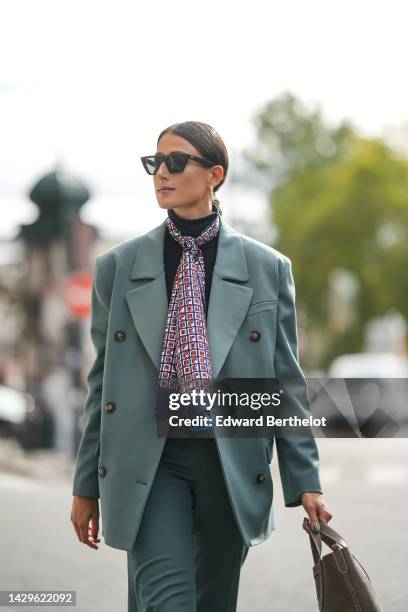 Julia Haghjoo wears black sunglasses, white pearls earrings, ,a black turtleneck pullover, a navy blue with camel and white print pattern silk scarf,...