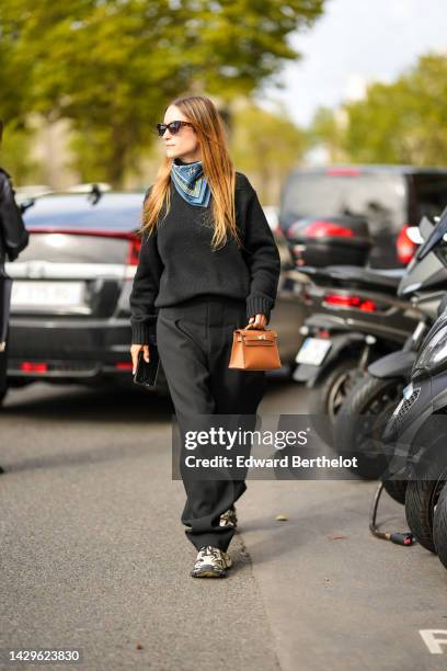 Charlotte Groeneveld wears black sunglasses, a pale blue and white print pattern silk scarf from Hermes, a black wool pullover, black large suit...