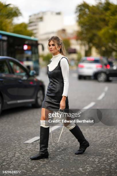 Xenia Adonts wears silver earrings, a white ruffled turtleneck pullover, a white ruffled V-neck / long sleeves pullover, a black shiny leather...