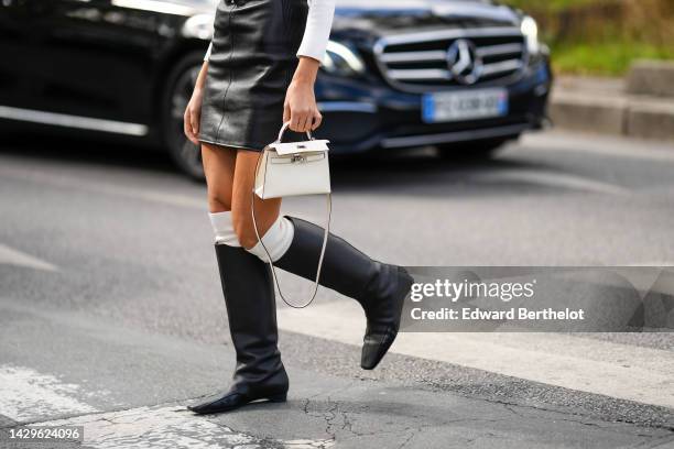 Xenia Adonts wears a white ruffled V-neck / long sleeves pullover, a black shiny leather tank-top / short dress, a white shiny leather mini Kelly...