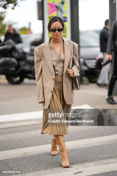 Aimee Song wears black sunglasses from Prada, gold chain pendants necklace, a white pearls necklace, a brown beige buttoned / v-neck gilet, a beige...