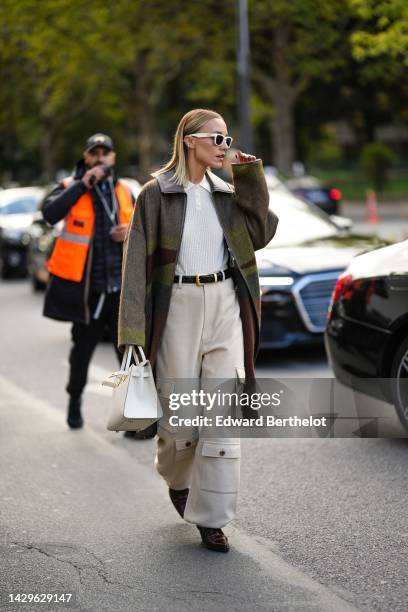 Viktoria Rader wears white latte sunglasses, silver and diamonds earrings, a white wool ribbed polo shirt, a khaki / gray / brown print pattern...