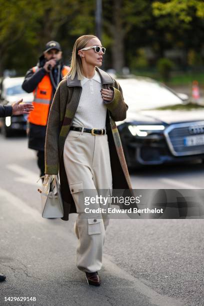 Viktoria Rader wears white latte sunglasses, silver and diamonds earrings, a white wool ribbed polo shirt, a khaki / gray / brown print pattern...