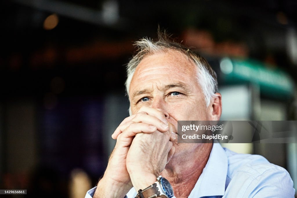 Handsome middle-aged man looking serious and thoughtful, resting his chin on his hands