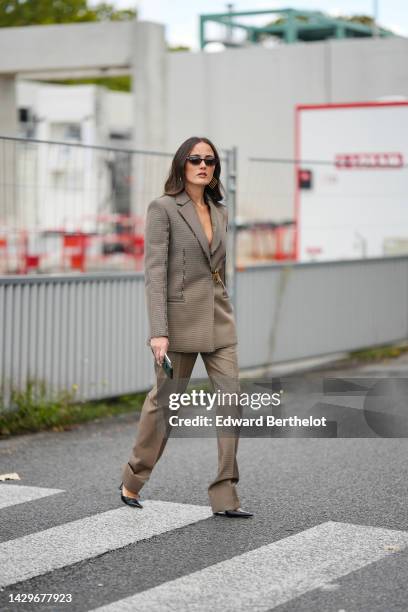 Guest wears black and brown sunglasses, gold large square earrings, a brown and black small checkered print pattern blazer jacket closed by a gold...