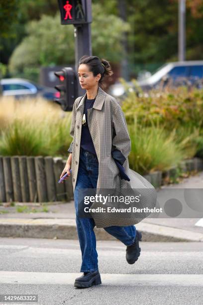 Guest wears a neon yellow hair elastic, a beige and black checkered print pattern long coat, a navy blue t-shirt, blue denim large pants, black shiny...